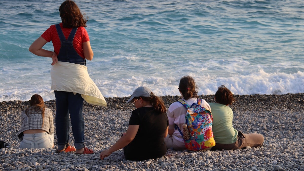 People sitting on a pebble beach by the ocean.